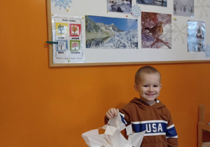 Chłopiec pozuje do zdjecia z papierową gwiazdą, W tle dekoracja zimowa