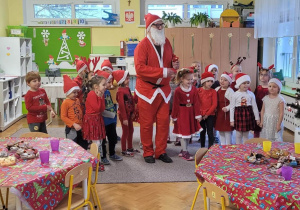 Grupa dzieci w czerwonych strojach pozuje do zdjecia z Mikołajem