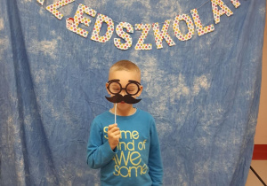 Chłopiec pozuje na niebieskim tle z napisem "dzień przedszkolaka" i akcesoriami do zdjęć