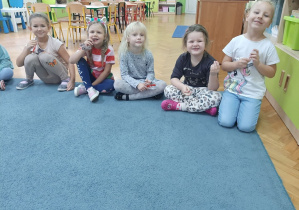 Dziewczynki siedzą na dywanie i uśmiechają się do zdjecia