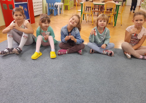 Dziewczynki siedzą na dywanie i jedzą czekoladowe batony, uśmiechają się do zdjecia