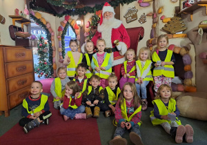Grupa dzieci pozuje do zdjęcia z Mikołajem w tle dekoracje o tematyce świątecznej