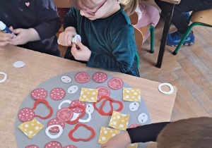 Dzieci siedzą przy stoliku i układają elementy na szablonie koła