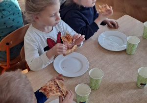 Dzieci siedzą przy stoliku i jedzą pizzę z pizzerii