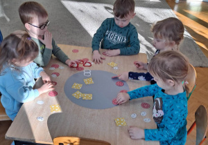 Dzieci siedzą przy stoliku i układają elementy na szablonie koła