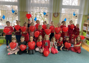 Grupa dzieci ubrana na czerwono pozuje do zdjęcia z sercami z balonów
