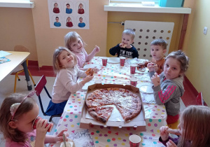 Dzieci siedzą przy stoliku u jedzą pizzę