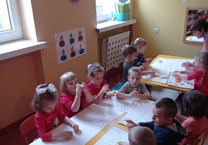 Dzieci siedzą przy stoliku i wyrabiają masę