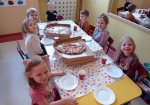 Dzieci siedzą przy stoliku u jedzą pizzę