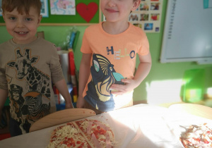 Chłopcy uśmiechają się do zdjęcia na stoliku leży pizza