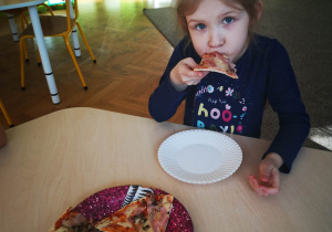 Dziewczynka siedzi przy stoliku i je pizze