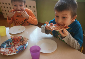 Chłopcy siedzą przy stoliku i jedzą pizze
