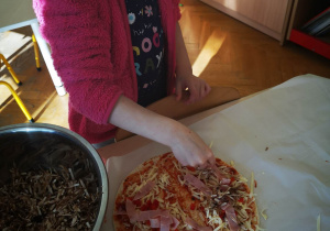 Dziewczynka samodzielnie przygotowuje pizzę i układa składnicy na cieście