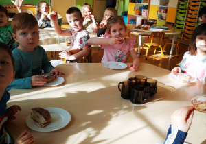 Dzieci siedzą przy stolikach i jedzą pączki