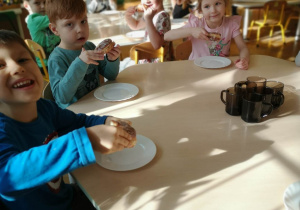 Dzieci siedzą przy stolikach i jedzą pączki