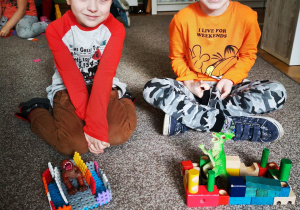 Chłopcy uśmiechają się do zdjecia i prezentują stworzone budowle dla dinozaurów