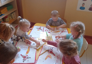 Grupa dzieci siedzi przy stoliku i maluje farbami