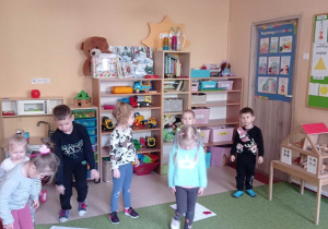 Dzieci biorą udział w zajęciach ruchowych w tle szafki z zabawkami
