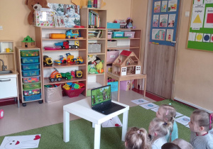 Dzieci siedzą na dywanie i oglądają film edukacyjny na laptopie