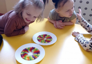 Dzieci przy stoliku obserwują doświadczenie z kolorowymi cukierkami