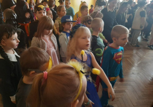 Dzieci w strojach karnawałowych tańczą na sali gimnastycznej w szkole