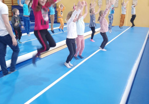 Dzieci skaczą na materacu w tle drabiki w sali gimnastycznej