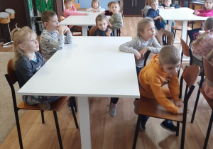 Dzieci siedzą przy ławkach w szkolnej sali