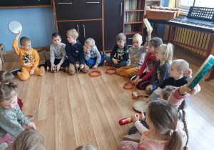 Dzieci siedzą w na podłodze i grają na różnych instrumentach
