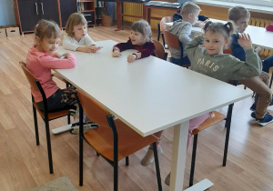 Dzieci siedzą przy ławkach w szkolnej sali