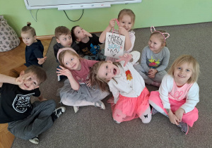 Grupa dzieci siedzi na dywanie i pozuje do zdjęcia