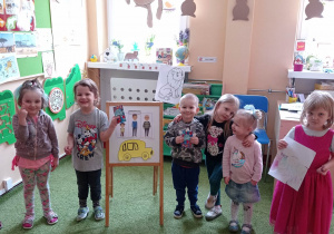 Grupa dzieci pozuje do zdjęcia, chłopcy trzymają upominki, w tle tablica z ilustracjami i dekoracje wielkanocne