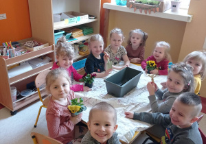 Dzieci siedzą przy stoliku u trzymają sadzonki bratków.