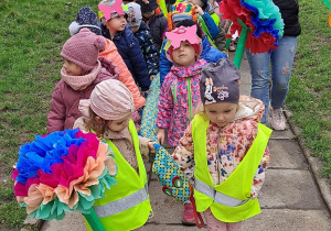 Dzieci maszerują po chodniku niosą w rękach kwiaty