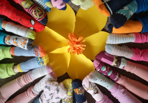 Stopy dzieci w kolorowych skarpetkach ułożone w okrąg, na środku papierowy kwiat