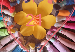 Stopy dzieci w kolorowych skarpetkach ułożone w okrąg, na środku papierowy kwiat