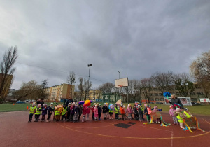 Grupa dzieci pozuje do zdjecia na boisku szkolnym w rękach trzyma transparenty i kwiaty z bibuły