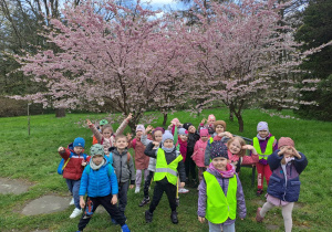 Grupa dzieci pozuje do zdjęcia na tle kwitnących drzew wiśni