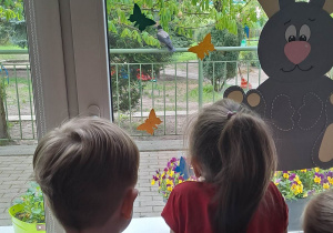 Dzieci wyglądają przez okno i obserwują wronę na drzewie