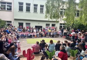 Przedszkolaki stoją w ogrodzie przedszkolnym i czekają na występ