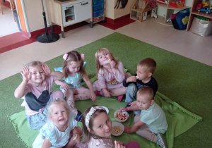 Dzieci siedzą na kocu i jedzą owoce