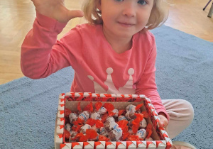 Dziewczynka trzyma pudełko cukierków i pokazuje na palcach ile mam lat
