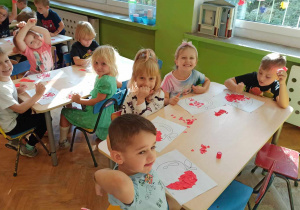 Dzieci przy stoliku wykonują prace plastyczną o tematyce jabłka