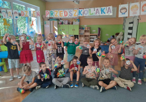 Grupa dzieci pozuje do zdjęcia z prezentami, nad nimi napis Dzień Przedszkolaka