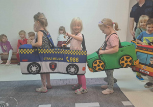 Dzieci przebrane za pojazdy poruszają się po dywanie z nadrukowaną ulicą