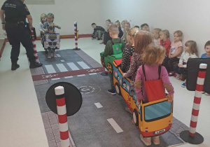 Dzieci przebrane za pojazdy poruszają się po dywanie z nadrukowaną ulicą