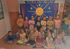 Grupa dzieci uśmiecha się do zdjęcia w tle dekoracja słońce i napis Dzień Uśmiechu