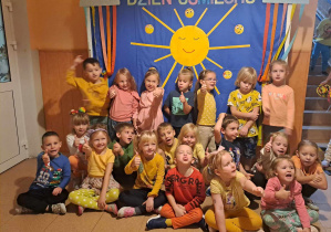 Grupa dzieci uśmiecha się do zdjęcia w tle dekoracja słońce i napis Dzień Uśmiechu