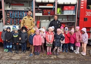 Grupa dzieci pozuje do zdjecia ze strażakami na tle wozu strażackiego