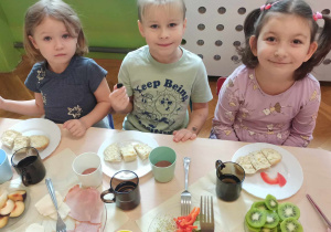 Dzieci siedzą przy stolikach i jedzą samodzielnie przygotowane kanapki