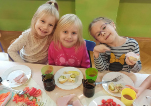 Dzieci siedzą przy stolikach i jedzą samodzielnie przygotowane kanapki